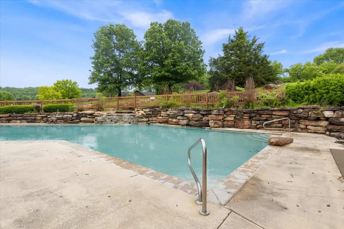 A tranquil outdoor pool area bordered by a rock wall and surrounded by vibrant greenery. The setting is ideal for sunbathing, swimming, or gathering with friends and family in a peaceful environment.