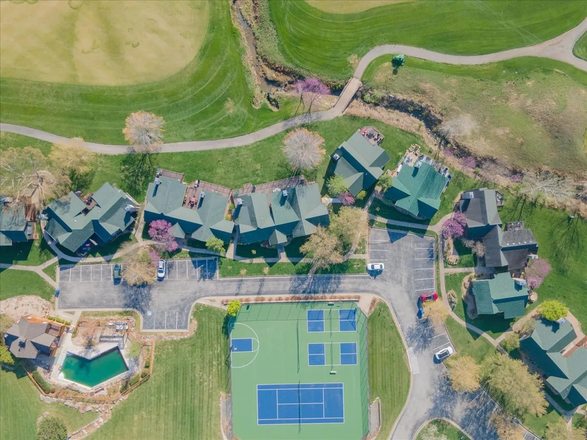 This exterior view highlights both the tennis courts and swimming pool, with surrounding green spaces and residential units in the background. The scene evokes a sense of community, activity, and accessible luxury.