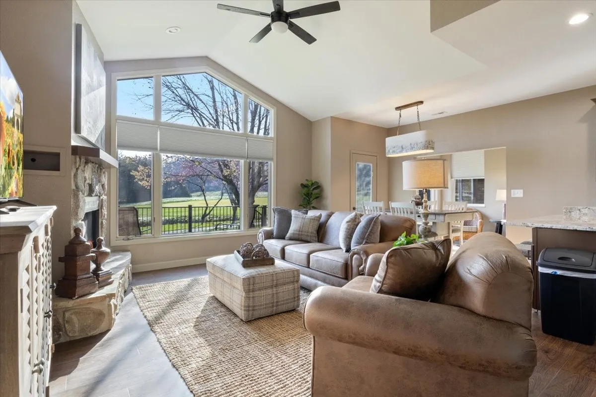A cozy living room with large windows offering views of the outdoors, comfortable seating arranged for conversation or watching TV, and a stylish coffee table as the focal point. The space is airy and bathed in natural light, fostering both relaxation and togetherness.