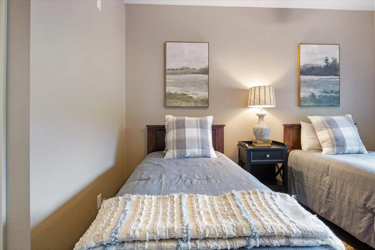 A cozy bedroom with two twin beds, decorative paintings above the headboards, and a soft table lamp between the beds. The décor is peaceful and the space exudes warmth and comfort, ideal for conversation or winding down after a busy day.