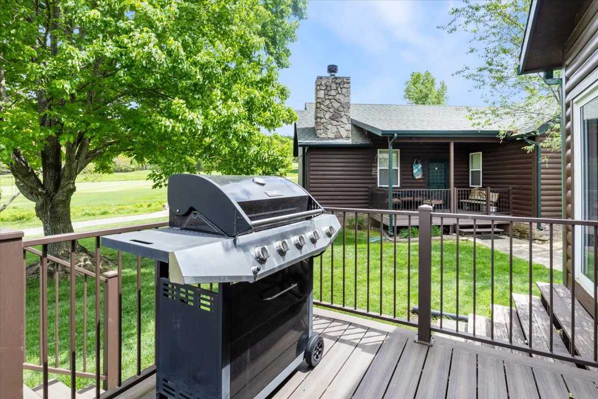 This image showcases a wooden deck with a grill, surrounded by green grass and a large tree, perfect for outdoor dining and barbecues. The inviting setup suggests a casual, friendly atmosphere for gatherings and socializing.